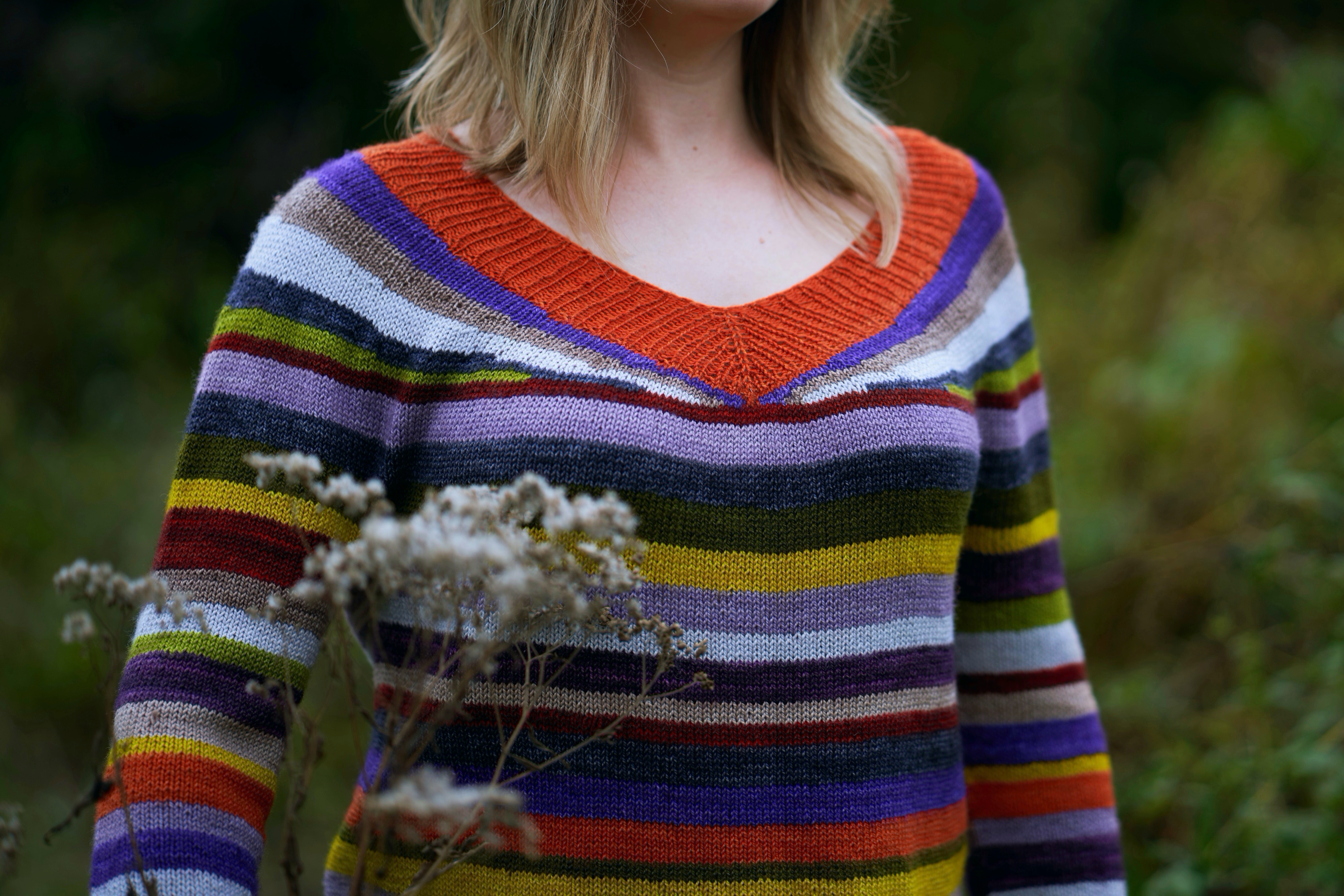 A closeup of a v-neck striped sweater knit in orange, green, purple, yellow and gray colors