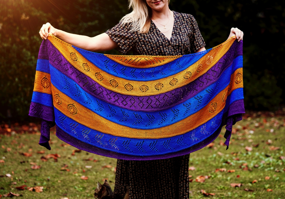 A woman holds a handknit lace Zodiac shawl